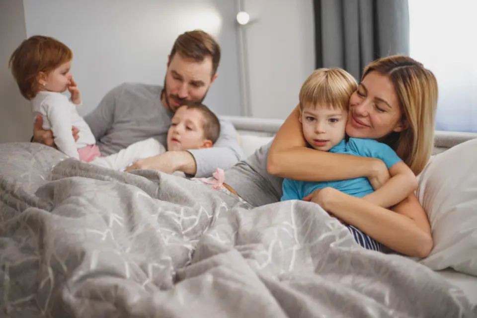A family with three young children together on a bed, laughing