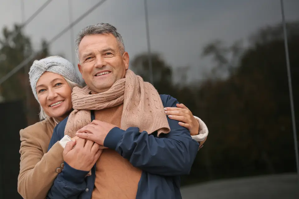 An older couple standing close together outdoors, both smiling