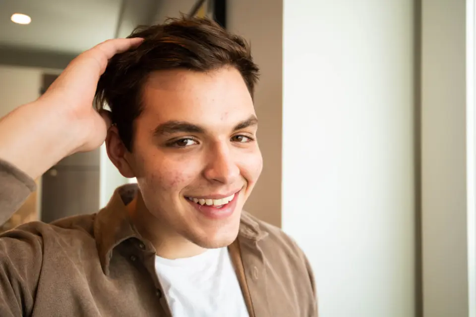 A young man laughing, one hand in his hair